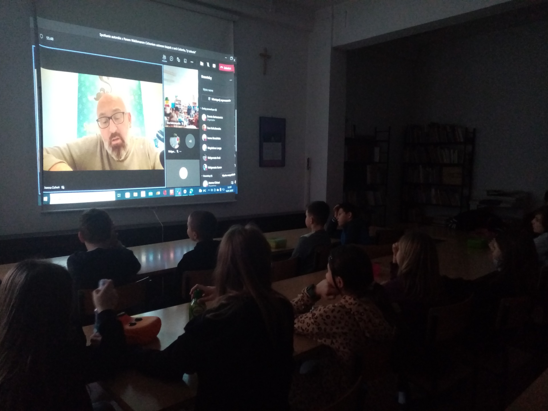 Klasa IV c słucha opowieści snutych przez autora książek z serii "Cukierku, Ty, łobuzie". Na ekranie widoczny autor.